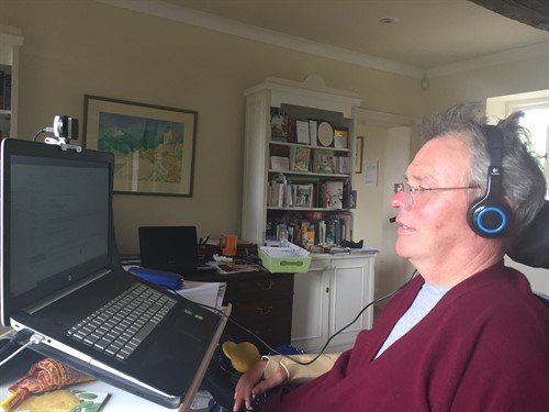 George, wearing a headset, sitting in front of a laptop computer and dictating to the computer. 