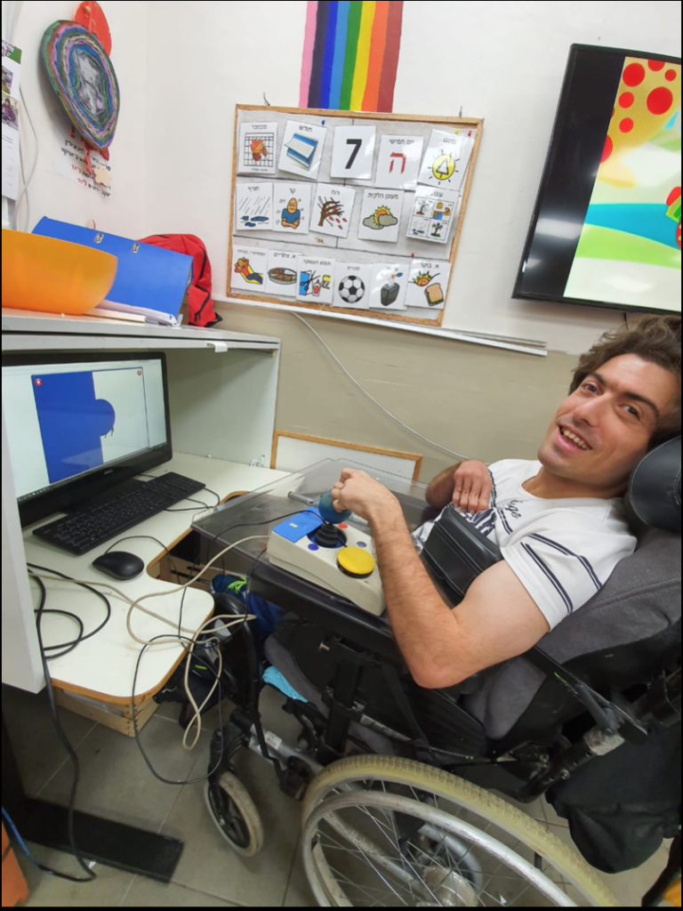 S, sitting in front of a computer operating it with a joystick