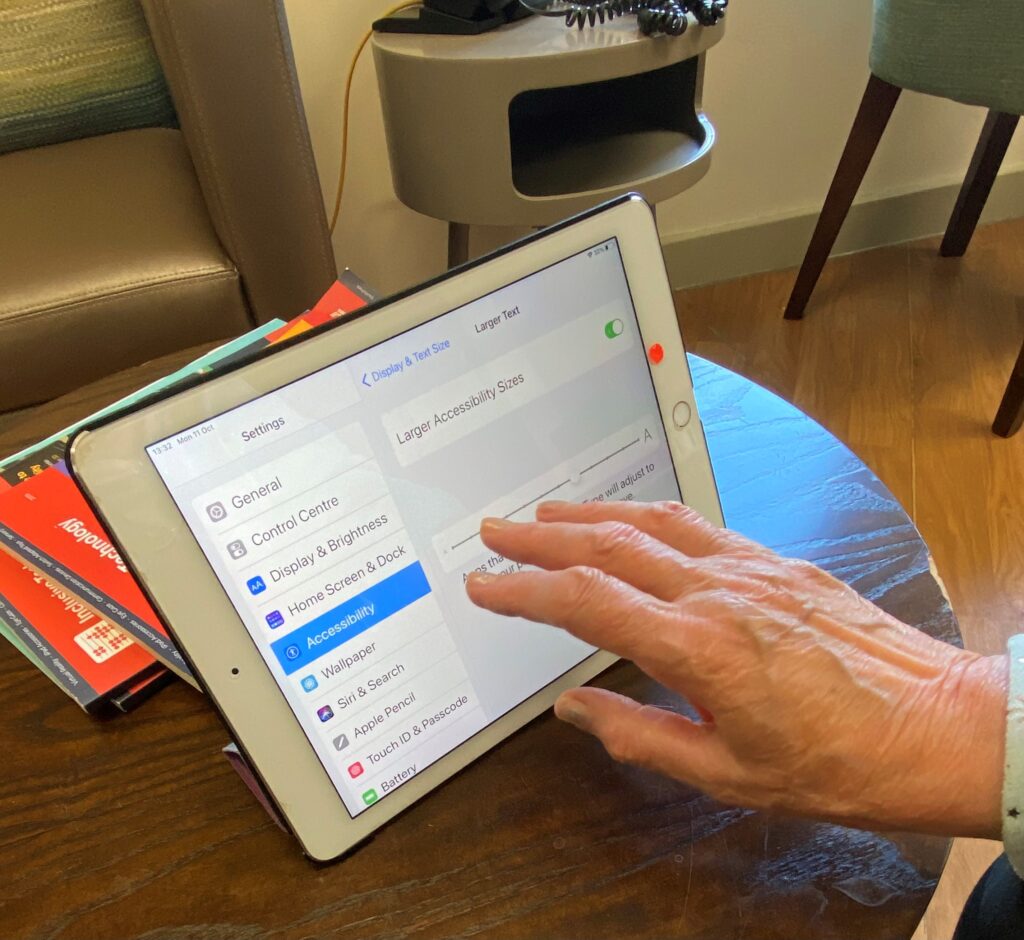 An iPad on a table with an old ladies hand touching the screen