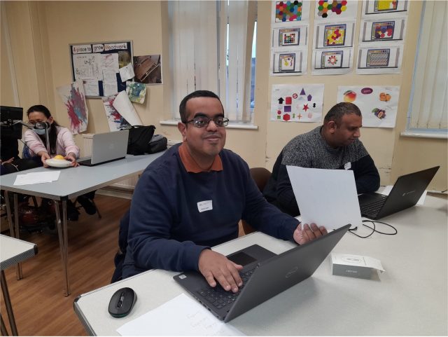A small group of happy students sitting at desks with laptops in front of them