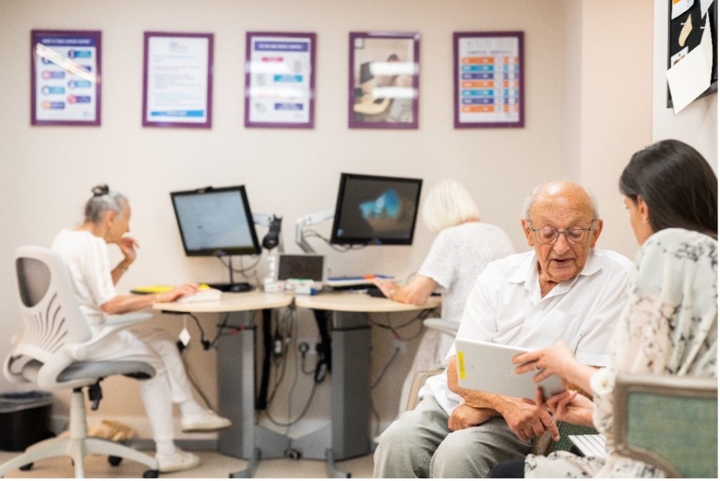 A group of elderly people sitting at a table with computers