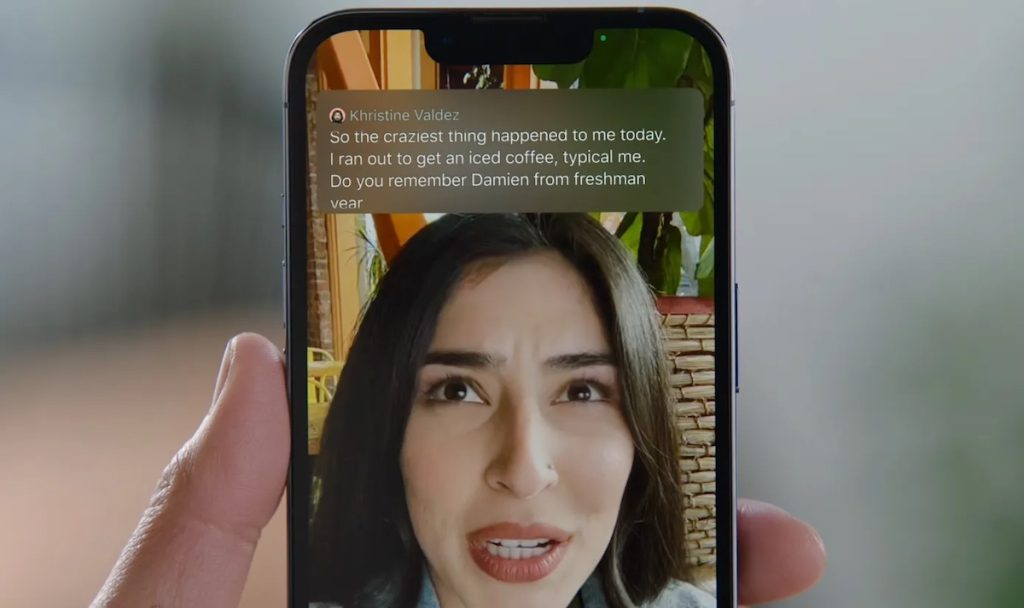 An iPhone showing a FaceTime call with a woman's face shown on the screen. Live captions of what she is saying appear on the screen above her head.  