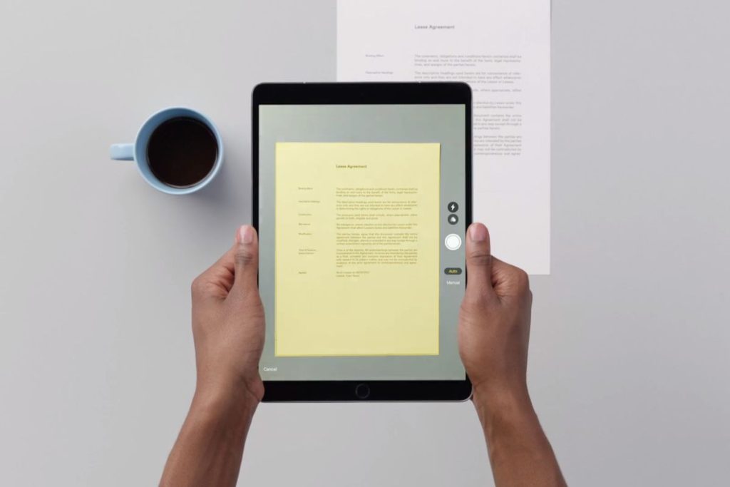 A person holding an iPad above a document on a table and using the iPad to scan the document