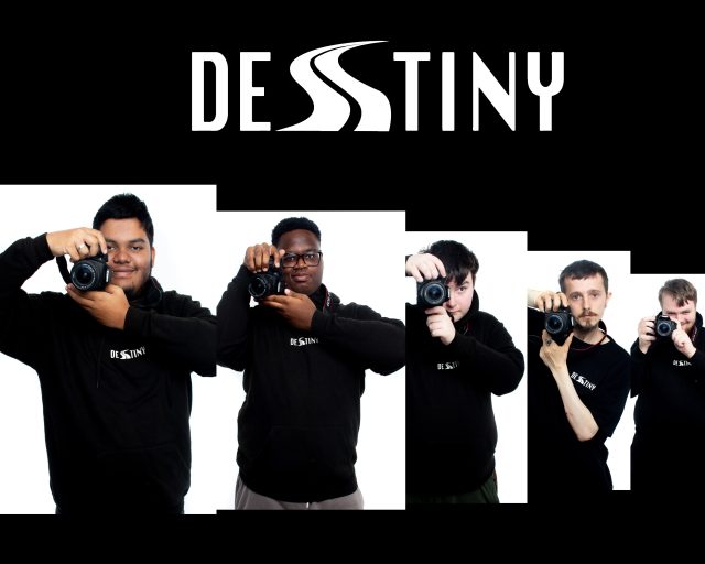 Group of Destiny enterprise students in black hoodies holding cameras, standing below a bold Destiny logo on a black background, representing their focus on videography and media skills.