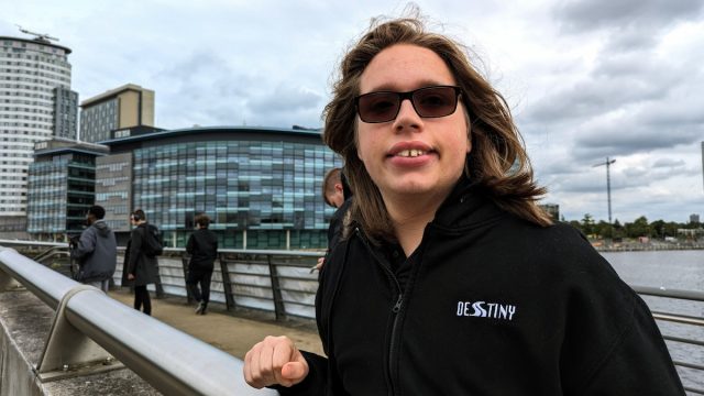 Max, a former student, smiling while standing on a bridge near Manchester’s MediaCity, wearing a black Destiny-branded hoodie.