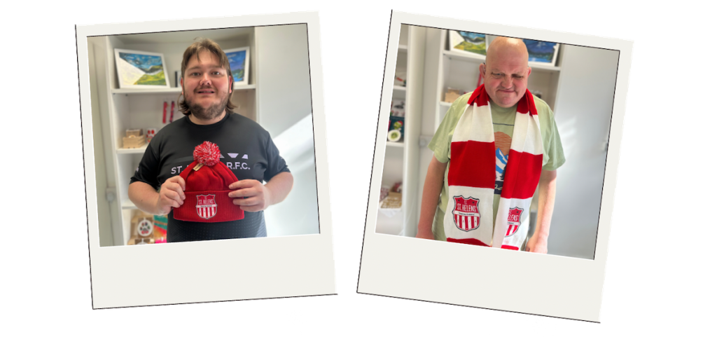 Two Buzz Hub team members proudly wearing and displaying finished FC St Helens merchandise - one holding a red bobble hat and the other wearing a red and white scarf.