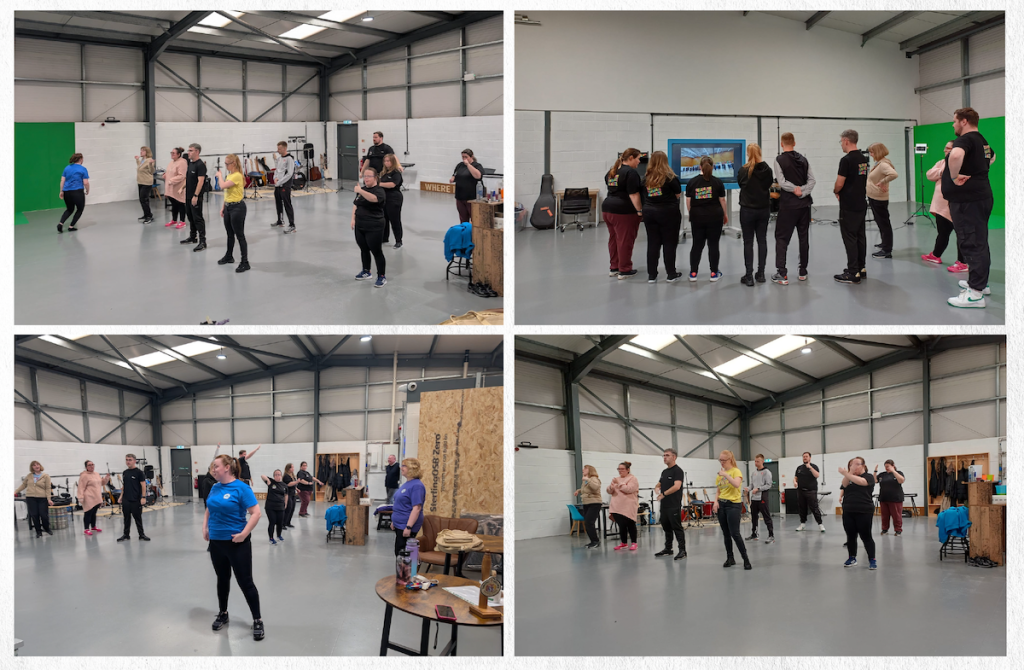 Everyone Move Collective members rehearsing choreography and reviewing footage in a large indoor studio space.
