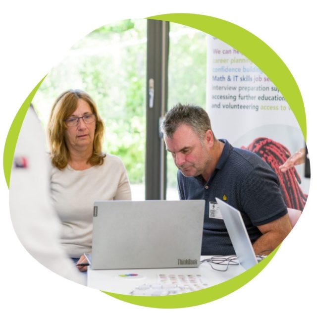 A man and woman are seated next to each other, facing a laptop.